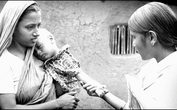 This volunteer smallpox eradication team vaccinator (right) was in the process of checking the smallpox vaccination scar on this young child’s left forearm, while he rested his head upon his mother’s shoulder
