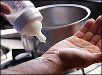 Photo of man testing temperature of milk in bottle.