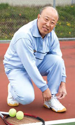 Photo of an elderly Asian man tying his shoes on a tennis court