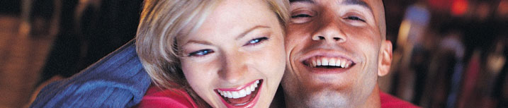 Close up image of a young adult man and a young adult woman embracing and laughing.
