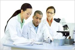 Three scientists reviewing information on paper in front of a microscope