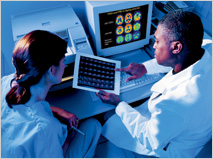 Two clinicians/scientists reviewing brain scan film, with PET scans shown on a computer monitor