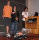 three students presenting their robot in the final competition and robotic vehicles are on the floor