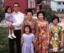 a family of Asian descent including 2 children and four adults standing in a yard with houses behind them