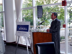 Man in gray suit speaking at podium with a sign that reads "Azercell" next to him.
