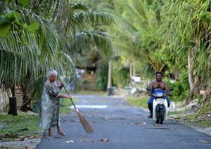 A woman sweeps road as a man passes on his scooter in Funafuti, Tuvalu, March 22, 2004. [© AP Images]