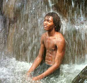 A man sits under waterfall near Soufriere, Saint Lucia, July 3, 1998. [© AP Images]
