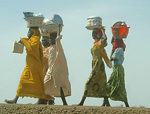 Women wearing traditionally patterned dresses walk with their goods to sell in N'djamena, Chad, February 22, 2006. [© AP Images]