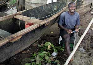 A man sits by canoe mending fishing nets in Santo Antonio on the island of Principe, November 8, 2006. [© AP Images]