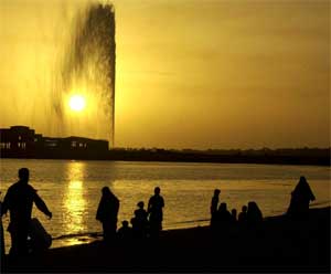Vacationers are silhouetted at beach in Jiddah, Saudi Arabia, with the landmark Jiddah fountain in background. May 7, 2004. [© AP Images]