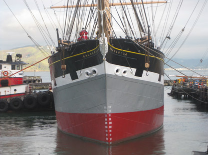The BALCLUTHA floating in the water with a tug boat pushing on her right (starboard) side to move her closer to the dock on her left (port) side.