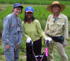 Enter the National Clearinghouse on Disability and Exchange pages here, Photo: Young woman with a walker stands in a field with two Japanese farmers