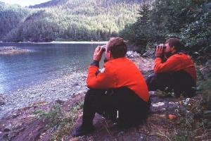 two people with binoculars looking out onto a body of water from the shore