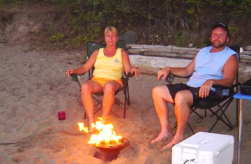 Visitors using an approved gas stove for shoreline camping. A woman and man sitting by a gas campfire on the beach.