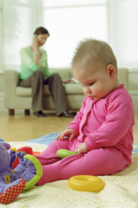 an infant playing on the ground while a women talks on the phone in the background