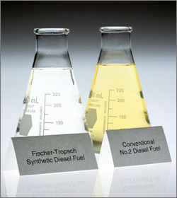 Photo showing a glass laboratory beaker or flask on the left containing a nearly clear liquid that is labeled as Fischer-Tropsch synthetic diesel fuel. Next to it is another glass flask containing a yellow liquid that is labeled as conventional number 2 diesel fuel.