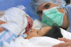 A picture of a woman holding an infant while her support person watches during a c-section