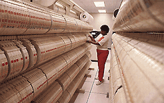 A woman retrieving a computer tape from the middle of an aisle containing shelves of computer tapes