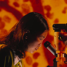 A picture of a woman looking into a microscope in front of a background of blood vessels.