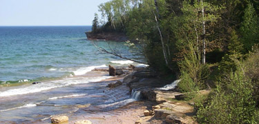 A waterfall trickles over the escarpment as the Pictured Rocks cliffs rise again after Miners Beach.