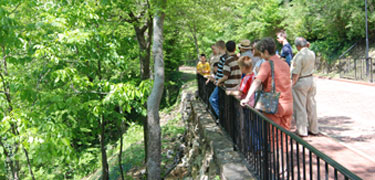 Ranger with tour group on brick promenade overlooking hot spring water cascade.