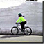 A bicyclist rides in front of a giant snowbank.