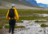 Photo of a hiker walking through a stream in the backcountry, with mountains in the background