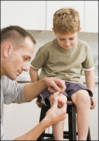 A father putting a bandages on his son's knee.