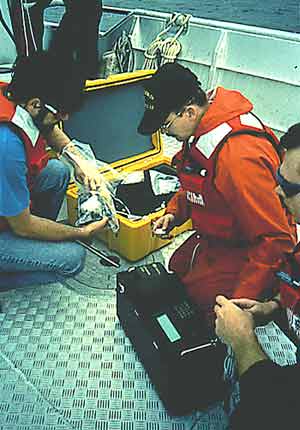 U.S. Coast Guard officers and a NOAA researcher preparing to deploy a fluorometer