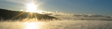 Sea fog rises over the water at sunrise.