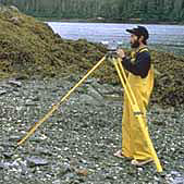 NOAA scientist examines a beach in Prince William Sound using a scientific instrument on a tripod.