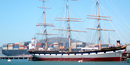Balclutha moored at the pier with a modern container ship passing behind her.