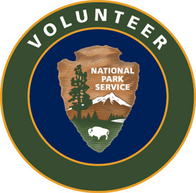 Volunteer in Parks logo. NPS arrowhead on a blue background ringed by green.