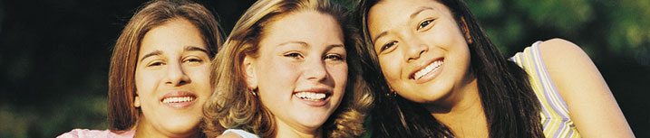 Close up image of three young women outdoors, smiling.