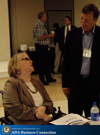 Photo:  Woman who uses wheelchair talks with man standing beside her.

