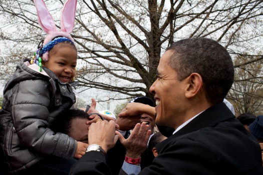 President Barack Obama smiles up at a young child in bunny ears