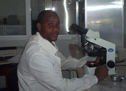 A male microscopist looking at the camera while sitting at his microscope.