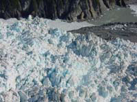 June 13, 2002, south-view from above the advancing terminus of Hubbard Glacier, of the mouth of Russell Fiord, showing the glacier margin and the push moraine that is blocked the entrance of the fiord. The push moraine is composed of sediment bulldozed from the floor of Russell Fiord by the advancing ice. Some of this sediment can be seen in contact with the bedrock on the south wall of the fiord. Water exiting Russell Fiord has cut a channel into the top of the moraine. USGS Photograph by Bruce F. Molnia (6/13/02-29).