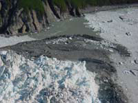 June 13, 2002, southwest-view from above the advancing terminus of Hubbard Glacier, of the mouth of Russell Fiord, showing the glacier margin and the push moraine that blocked the entrance of the fiord. The push moraine is composed of sediment bulldozed from the floor of Russell Fiord by the advancing ice. Some of this sediment can be seen in contact with the bedrock on the south wall of the fiord. Water exiting Russell Fiord has cut a channel into the top of the moraine. USGS Photograph by Bruce F. Molnia (6/13/02-30).