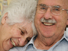Photo of a happy senior couple, the woman with her head on his shoulder.
