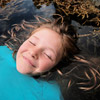 close up photo of a girl with her eyes closed, only her face above water and her hair swirling around