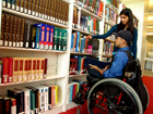 Male in wheelchair receiving assistance from female librarian.