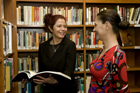 Two females standing having a conversation in a library.