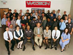 About forty workers posing for a group portrait in front of a Watson sign