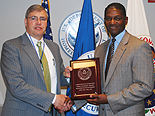 Dr. Peter Fonash (left), the Department of Homeland Security’s Acting Deputy Assistant Secretary for Cybersecurity and Communications, presents a plaque to National Communications System Chief of Staff Allen F. Woodhouse, marking the 25th Anniversary of the National Coordinating Center (NCC) for Communications during ceremonies in Arlington, April 6. (Photo by Steve Barrett, NCS)