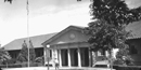 Black and white photo of the Government Free Bathhouse with a ranger walking on the sidewalk in front.