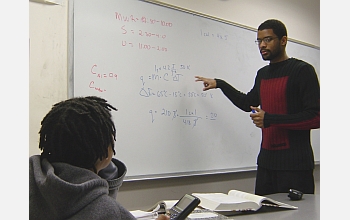 Student at white board works with other student on math problem