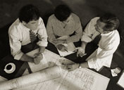 Image of business men and women sitting at a table and discussing housing blueprints.
