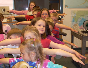 Children standing in line with their arms out to their sides.