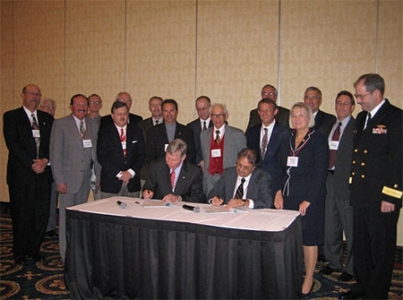Seated from left to right at the signing table are:  Malcolm P. Branch, President, Virginia Ship Repair Association and Leo Edwards, Acting Area Director, OSHA Norfolk Area Office.  Standing to the right of the signing table: U. S. Congresswoman, Thelma Drake and RDML John Clarke Orzalli.  Standing behind the signatories are several of the Partnership participants